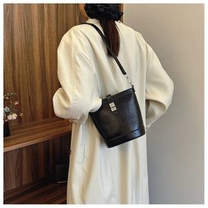 Detail of black leather bucket bag with silver clasp worn over a white coat