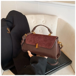 Détail du sac bandoulière vintage avec rabat en daim et boucle dorée posé sur une chaise