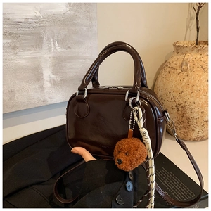Detail of dark brown glossy leather handbag with cute plush poodle charm on wool fabric