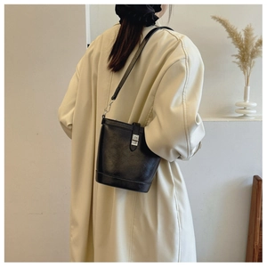 Minimalist black leather bucket bag with silver twist lock shown on model with beige coat