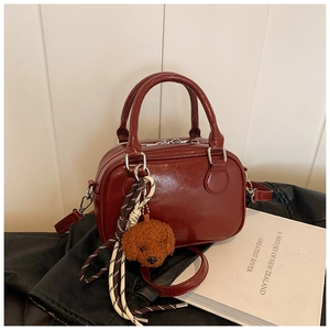 Detail view of a burgundy leather handbag with plush dog charm and silver hardware