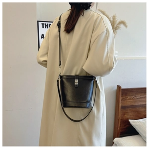 Detail of a black bucket bag featuring a sleek metal buckle and reinforced stitching