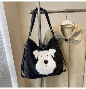 Détail d'un sac cabas en peluche noire avec un écusson de chien blanc sur un cintre