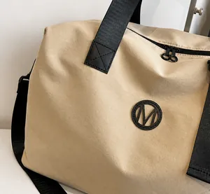 Detailed close-up of beige waterproof travel bag featuring soft fabric and M logo