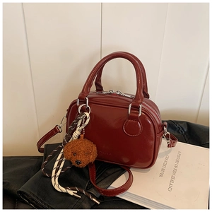 Macro view of wine red leather handbag with cute bear charm and woven keychain detail