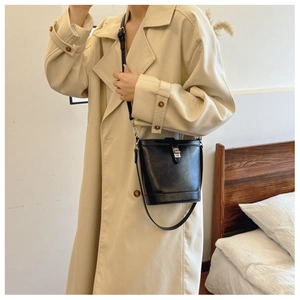Detail shot of a black leather bucket bag with silver clasp styled with a beige coat