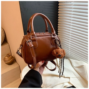 Detailed view of a brown leather Boston handbag with a plush bear charm and adjustable strap