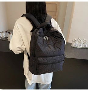 Rückansicht eines Modells mit schwarzem gestepptem Rucksack und silbernen Reißverschlüssen
