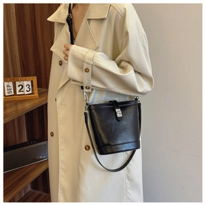 Detail of a black glossy bucket bag with metal clasp worn with a beige coat
