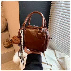 Brown faux leather Boston bag with plush bear charm and striped cord on a blazer background
