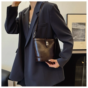 Detail of dark brown glossy leather bucket bag with silver rotating clasp worn by a model