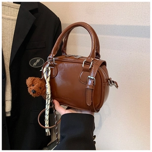 Detailed view of brown retro handbag with dual zippers and plush teddy bear charm accessory