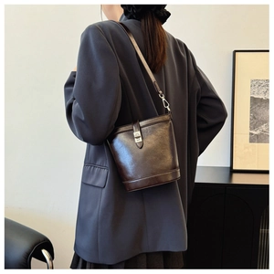 Detail of dark brown bucket bag with silver twist lock shown on grey casual blazer