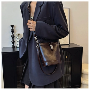 Close-up of a dark brown glossy leather bucket bag featuring a silver metal twist lock