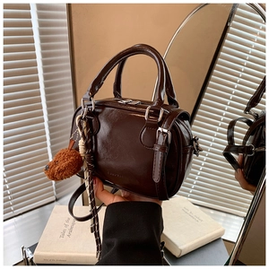 Detail of dark brown glossy Boston bag with logo, charm, and detachable shoulder strap