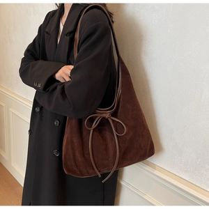 Detail of dark brown suede hobo bag with ribbon bow worn over a black wool coat