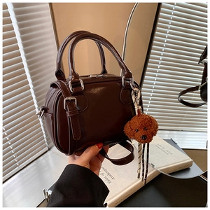 Detail of dark brown patent leather Boston bag with plush bear charm and glossy finish