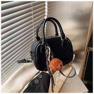 Macro detail of glossy black mini barrel bag with cute plush teddy bear charm accessory