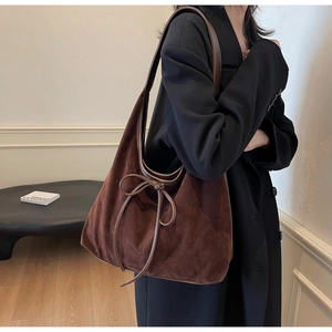 Detail of brown suede hobo bag with leather bow decoration on the side and wide strap