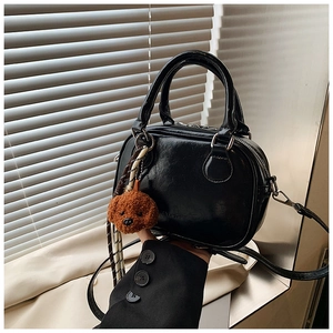 Detail of black crossbody square bag with brown plush puppy charm and glossy finish