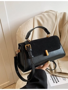 Sac à main noir en cuir et daim avec fermoir doré tenu sur fond de costume beige neutre