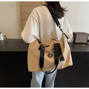 Detail of beige canvas travel bag with M logo and durable black woven nylon handles