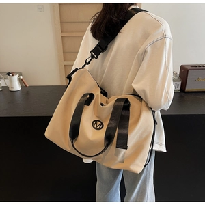 Khaki large capacity travel bag with black handles and M logo shown in a cafe setting
