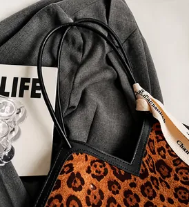Dettaglio della borsa tote leopardata con manici in pelle nera e ampia tracolla a nastro