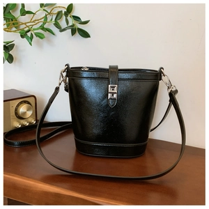 Detail of black glossy bucket bag with silver clasp lock on a vintage wooden table
