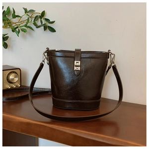 Detail of dark coffee leather bucket bag featuring a silver twist lock on a wooden desk