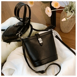 Detailed view of black textured leather bucket bag with silver metal twist lock on fabric