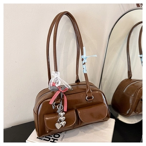 Detail einer braunen Ledertasche mit zwei Fronttaschen und dekorativen Schleifenanhängern