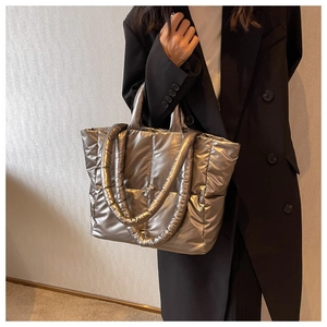 Detail of silver metallic quilted puffer tote bag shown on a model in a minimalist setting