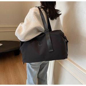 Rear view of a model carrying a large black waterproof nylon duffel bag with a round M logo