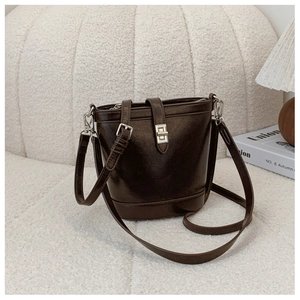 Detail view of dark brown glossy leather bucket bag with silver buckle and adjustable strap