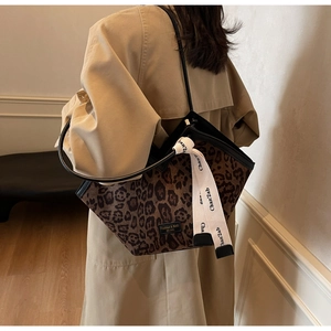 Dettaglio della borsa tote leopardata con nastro intrecciato e placca del marchio sul trench