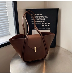 Détail d'un sac cabas en cuir marron avec côtés en forme d'ailes et fermoir doré en métal