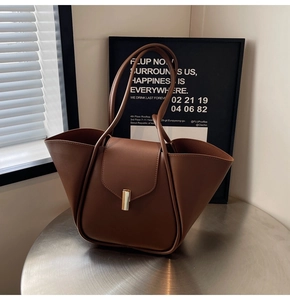 Détail d'un sac cabas en cuir marron avec structure pliée en ailes et boucle dorée