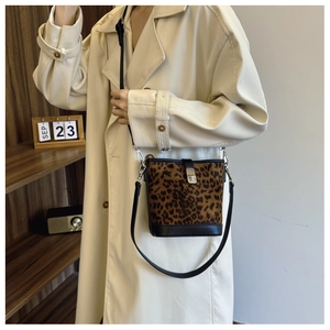 Detail of leopard print bucket bag with silver lock and black leather strap worn with beige coat