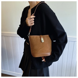 On-body shot of a vintage brown suede bucket bag with gold lock and sleek shoulder strap
