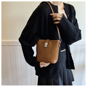 Detail of a brown suede and leather bucket bag with a silver twist lock on a model