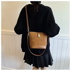 Detail of brown suede bucket bag featuring metal buckle and textured patchwork design