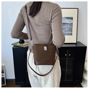 Detail of dark brown suede bucket bag with silver clasp shown on a model