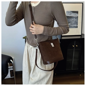 Close-up of brown suede bucket bag with silver metal clasp worn by a fashion model