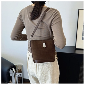 Close-up of brown suede bucket bag featuring silver metal twist lock and leather strap
