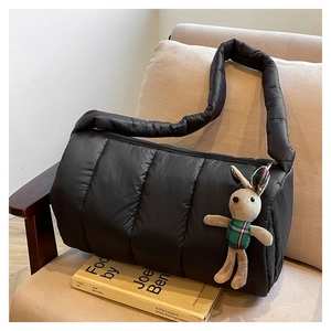 Detailed shot of black quilted puffer bag on sofa with cute beige rabbit plush charm