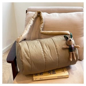 Quilted puffer shoulder bag in khaki nylon with a plush rabbit charm on a sofa