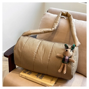Detail of khaki quilted puffer bag with plush bunny charm on a beige fabric sofa
