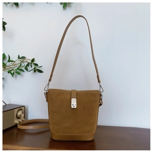Close-up of brown suede bucket bag featuring circular metal lock and dual straps