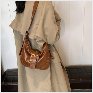 Nahaufnahme der braunen Retro-Schultertasche mit Silberschnalle über einem beigen Trenchcoat